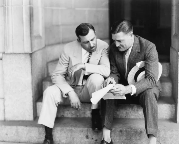 Δύο άνδρες συνεδρίαση στα σκαλοπάτια και την ανάγνωση ενός εγγράφου — Φωτογραφία Αρχείου