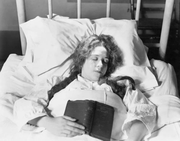 Mujer joven acostada en la cama, durmiendo y sosteniendo un libro — Foto de Stock