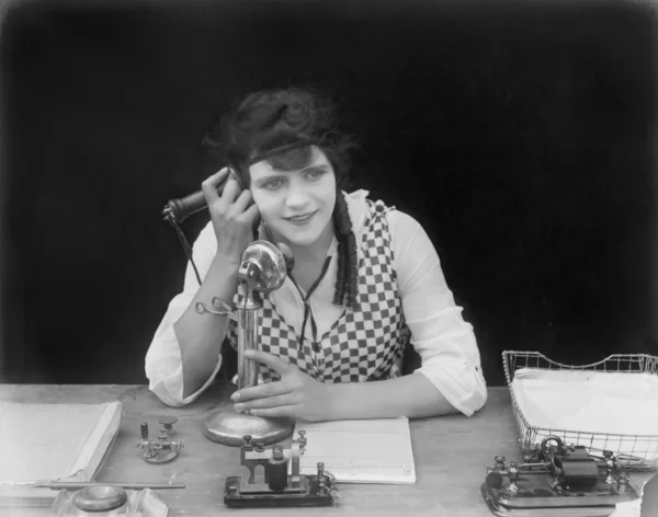 Ung kvinna sitter vid hennes skrivbord i ett kontor med en telefon i hennes händer — Stockfoto