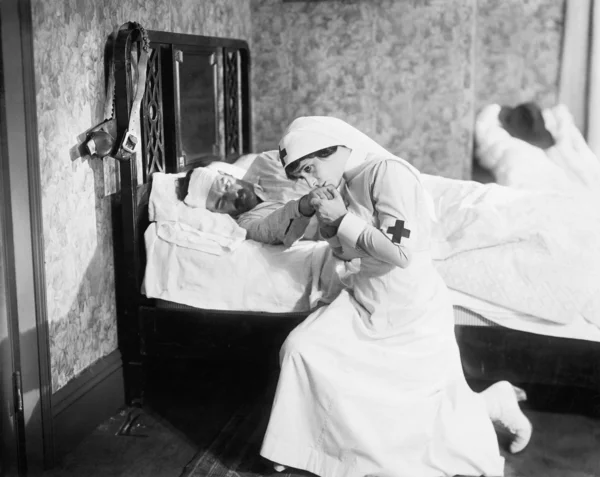 Verpleegkundige bidden voor een outlaw liggend in bed — Stockfoto