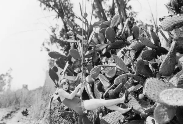 Молодая женщина висит на веревке рядом с большими растениями кактуса — стоковое фото