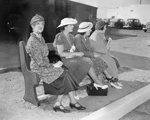 Четыре женщины сидят на скамейке и ждут автобус. — стоковое фото