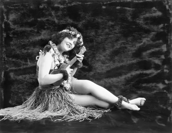 Νεαρή γυναίκα που παίζει κιθάρα σε μια Χαβάης χόρτο φούστα — Φωτογραφία Αρχείου