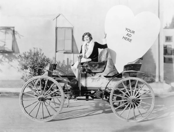 Młoda kobieta siedzi na samochód, posiadający wielkie serce w kształcie znak — Zdjęcie stockowe