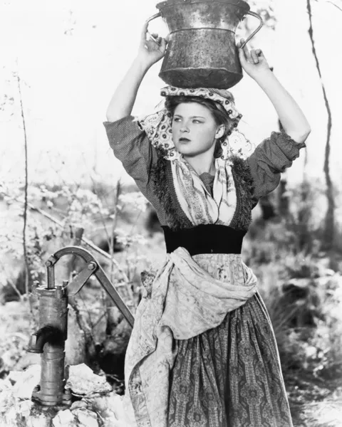 Молодая женщина с ведром воды на голове рядом с колодцем — стоковое фото