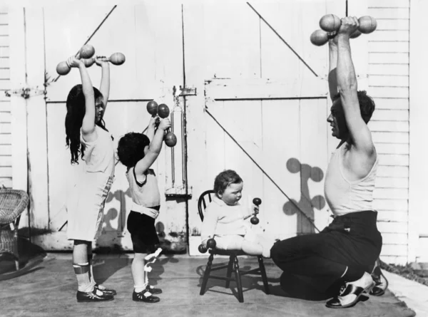 Pai e seus três filhos tendo um treino com halteres — Fotografia de Stock