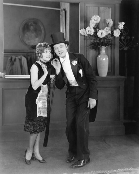 Продавец пальто шепчет человеку в цилиндре
