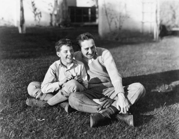 Otec a syn spolu sedí v trávě na dvorku — Stock fotografie