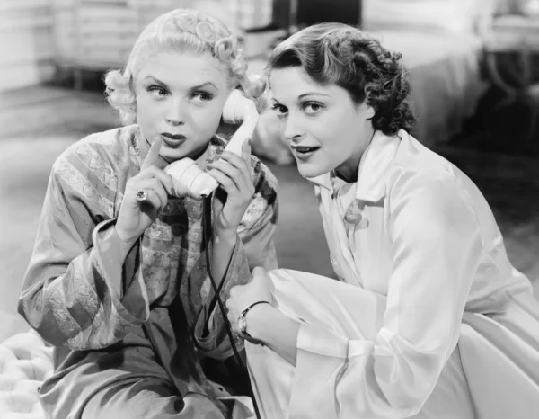 stock image Two women sitting together and listening on the telephone receiver