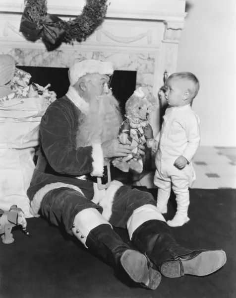 Weihnachtsmann mit einem kleinen Jungen und einem Teddybär vor einem Kamin — Stockfoto