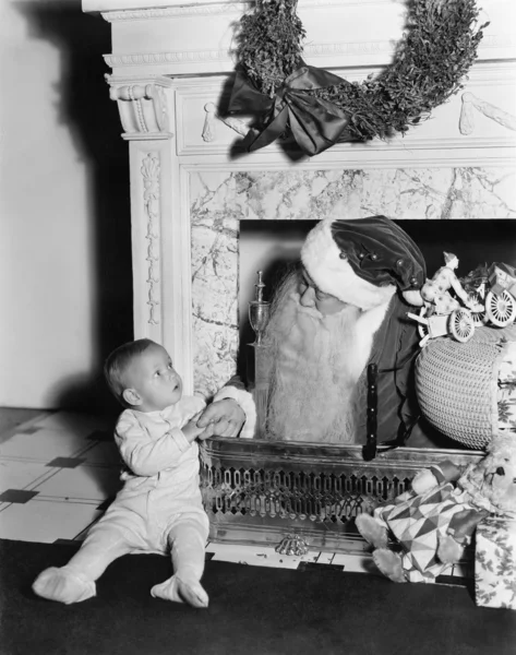 Jultomten med en liten pojke framför en öppen spis — Stockfoto