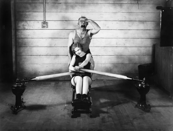Γυναίκα που κάθεται σε μια μηχανή κωπηλασίας με έναν άνδρα πίσω της — Φωτογραφία Αρχείου
