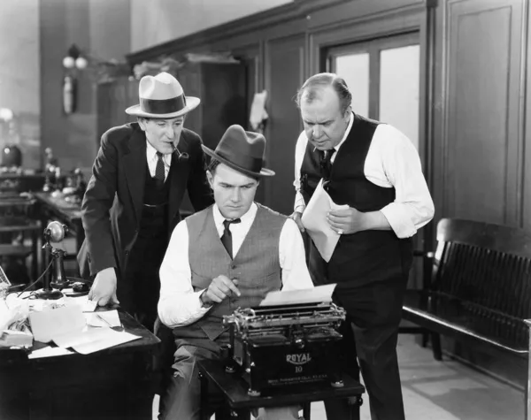 Três homens em um escritório curvado sobre uma máquina de escrever — Fotografia de Stock