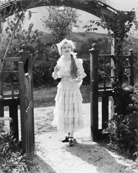 Mujer joven con un vestido blanco, caminando por un arco — Foto de Stock