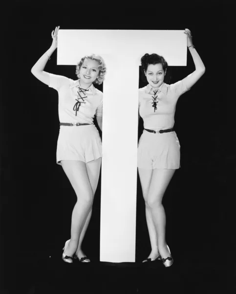 Mujeres posando con enorme letra T Imagen de stock