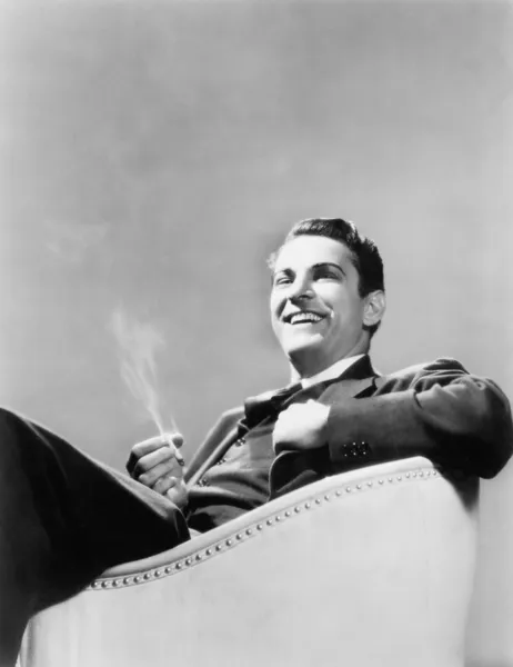 Человек, сидящий в кресле и курящий Стоковая Картинка