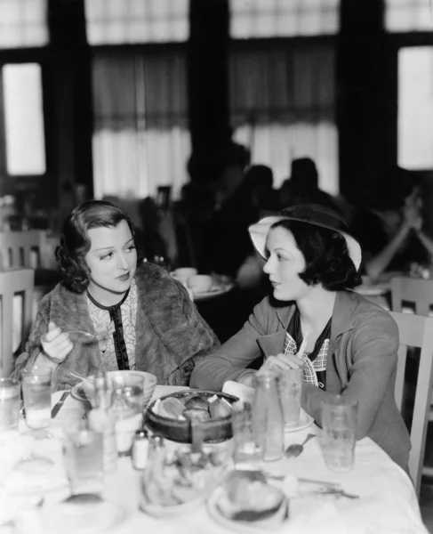 Two young women sitting in a restaurant and looking at each other Stock Image