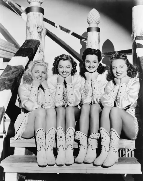 Retrato de quatro jovens mulheres sentadas em degraus em roupas ocidentais Fotografia De Stock