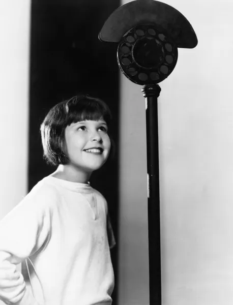 Profil av en ung flicka tittar på en mikrofon och ler Stockbild