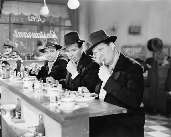 Three men with hats eating at the counter of a diner Stock Image
