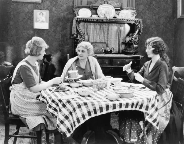 Drie vrouwen zitten op de eettafel te praten Stockfoto