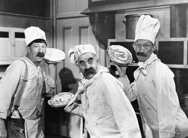 Three chefs holding pies for a fight in the kitchen Royalty Free Stock Images