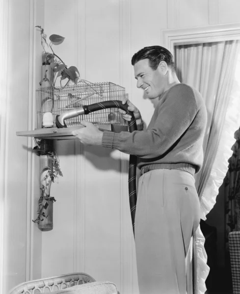 Perfil de um homem limpando uma gaiola com um aspirador de pó Imagens Royalty-Free
