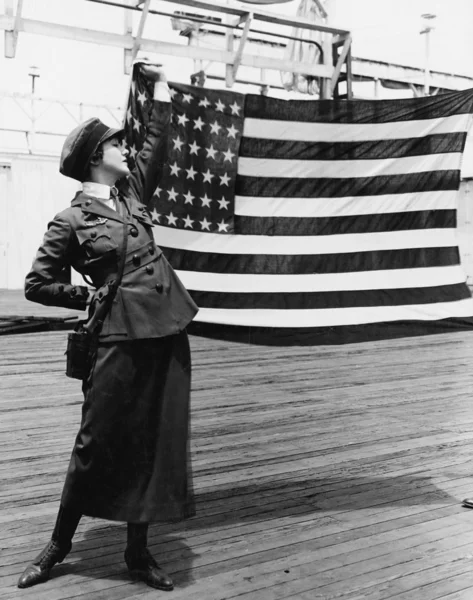 Young woman in military uniform holding up an American flag — Stock Photo, Image