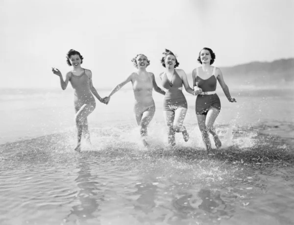 Vier vrouwen lopen in water op het strand Stockafbeelding