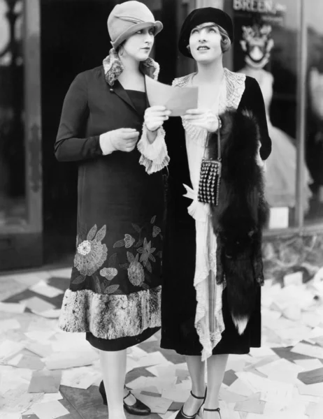 Two women in the street reading papers being thrown down from an office Stock Photo