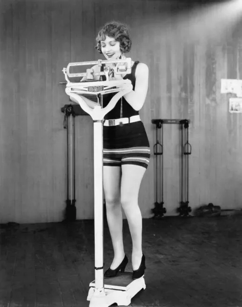 Junge Frau auf einer Waage, die ihr Gewicht nimmt lizenzfreie Stockbilder