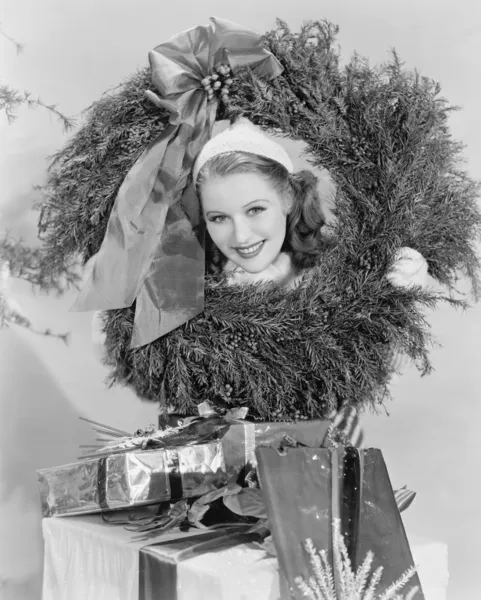 Young woman looking through a wreath with presents in front of her Stock Photo