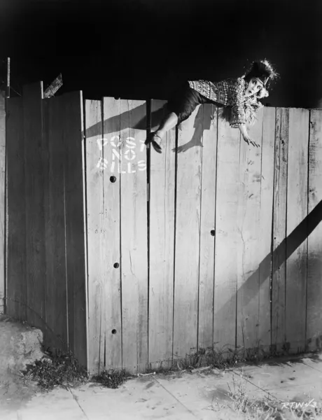 Young woman trying to climb over a wooden fence — Stock Photo, Image