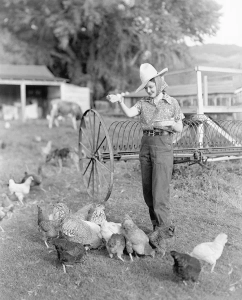 Junge Frau als Bäuerin verkleidet, die den Hühnern Futter bringt — Stockfoto
