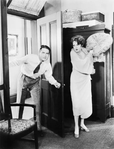 Frau steht hinter einer Tür und versucht, einen Mann mit einem Kissen zu schlagen Stockbild