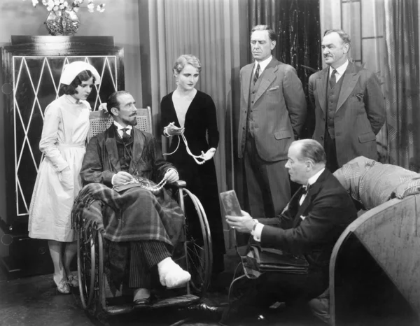 Man in a wheel chair with a broken foot and a group of — Stock Photo, Image