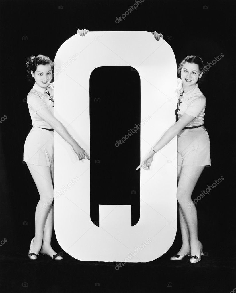 Two women pointing at huge letter Q