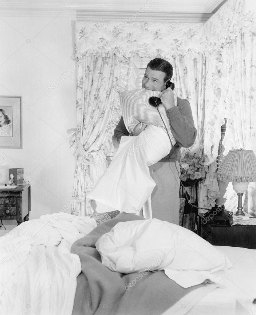 Young man talking on the telephone and biting into a pillows