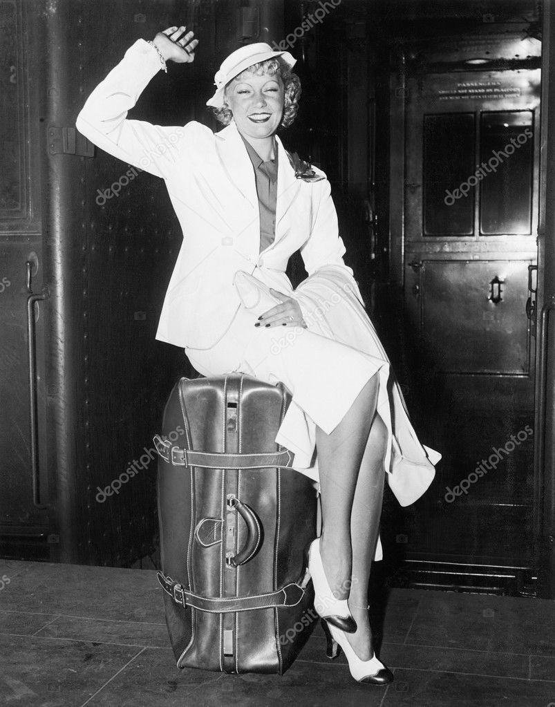 A ready to go young woman sitting on her suitcase and waving