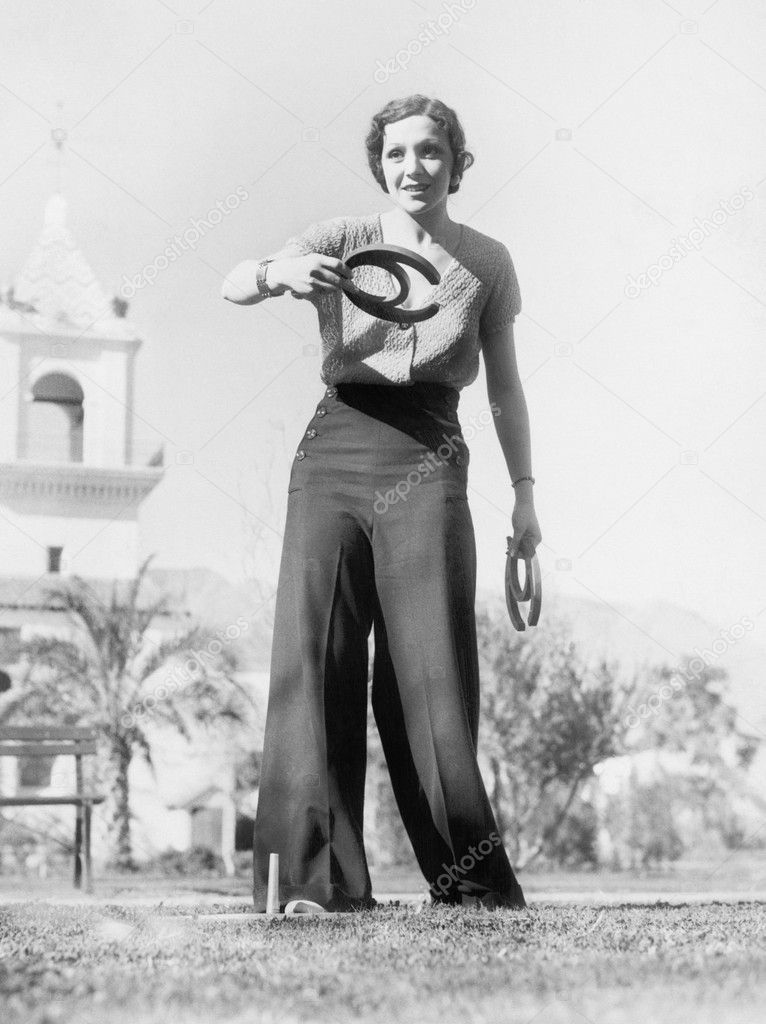Young woman in a yard, playing horse shoes, aiming for a lucky toss