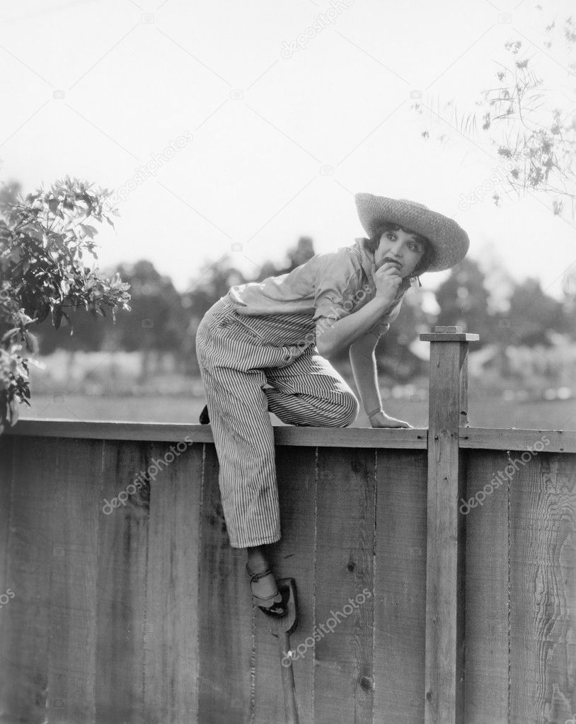 Young woman trying to get over a wooden fence with a fruit in her hands