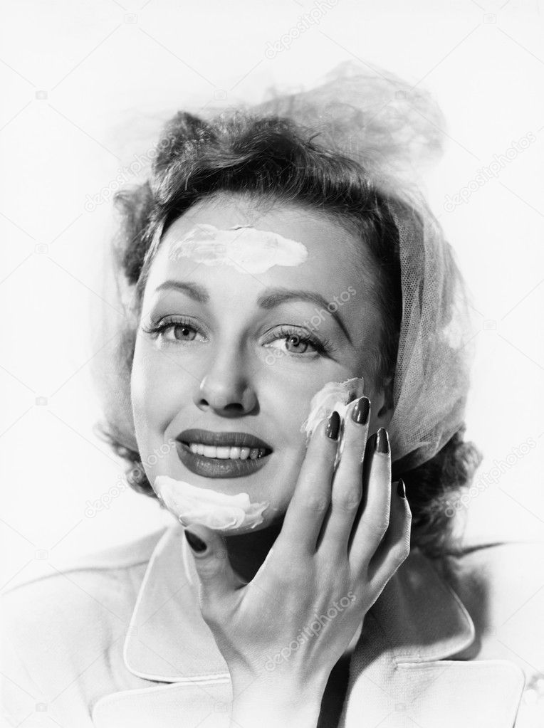 Young woman putting cream onto her face