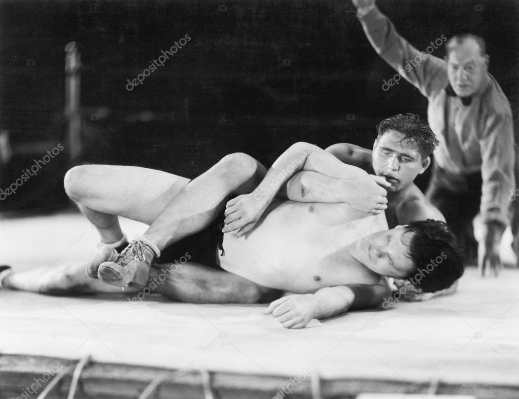 Two men wrestling with a referee in the background