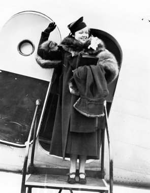 Elegant woman stepping out of an airplane and waving clipart