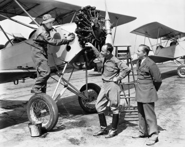 Three men standing next to an aircraft having a conversation clipart