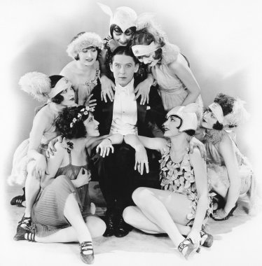 Young man sitting with a group of young women around him clipart