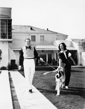 Couple walking their St. Bernard outside their home clipart