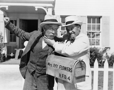 Two mature men fighting near a mail box in front of a house clipart