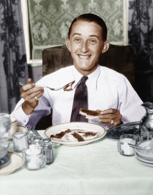 Young man having breakfast and smiling clipart