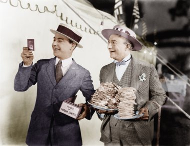 Man holding plates of sandwiches with a man looking at a film slide beside him clipart